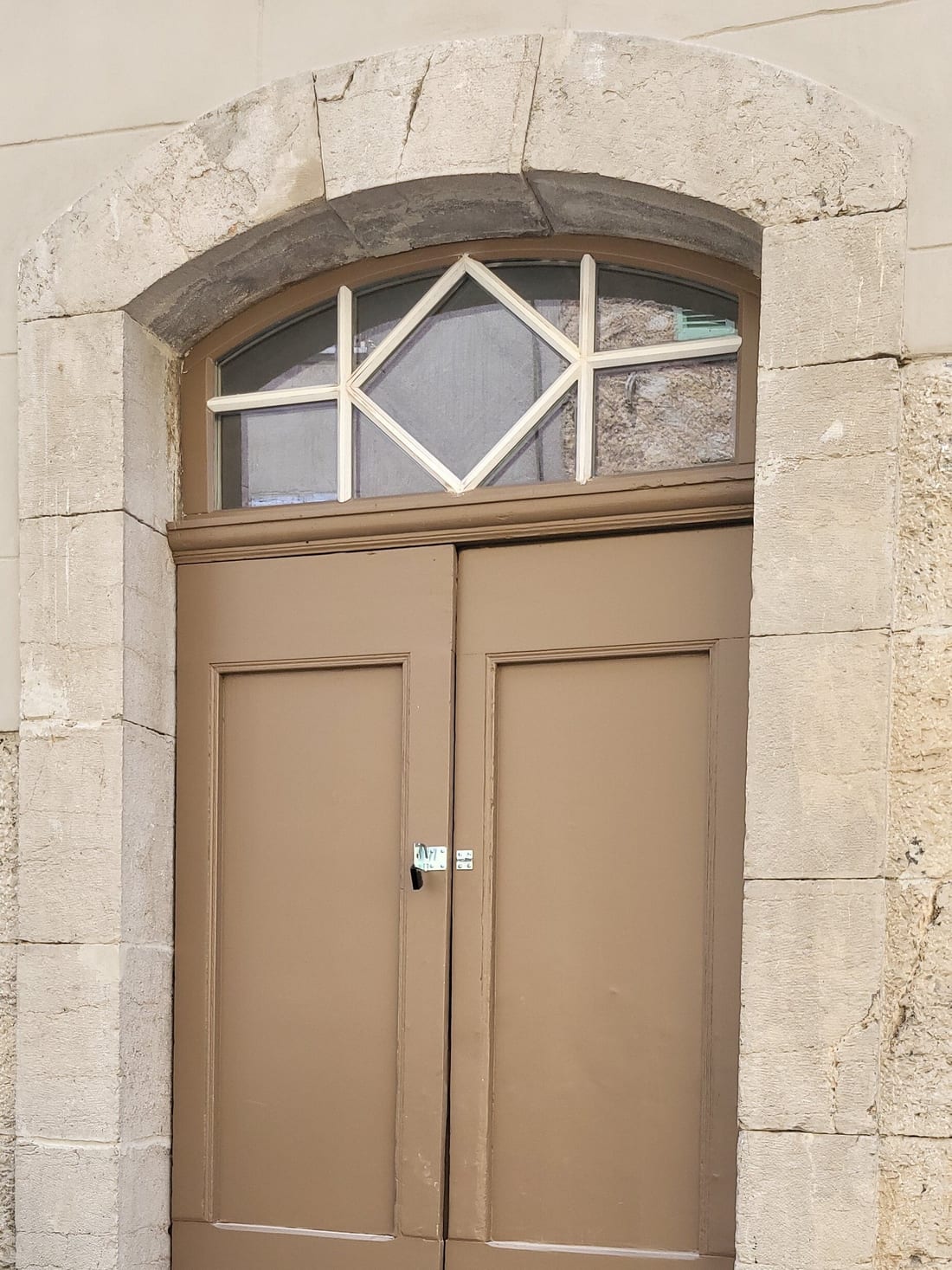 Porte cochère à deux vantaux et imposte cintrée à croisillons dans un encadrement en pierre de taille